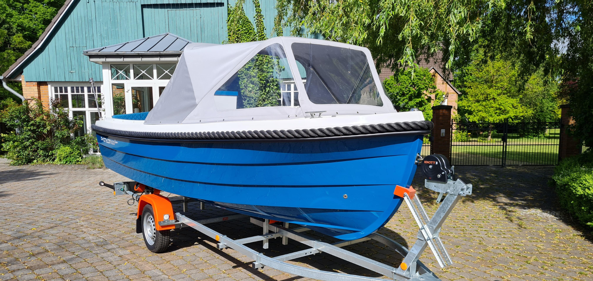 Motorboot Phantom 500 Classic in der Sonderlackierung Azurblau mit grauer Sprayhood. Das Boot steh auf einem neuem Bootstrailer mit Sliprollen und Bugwinde.